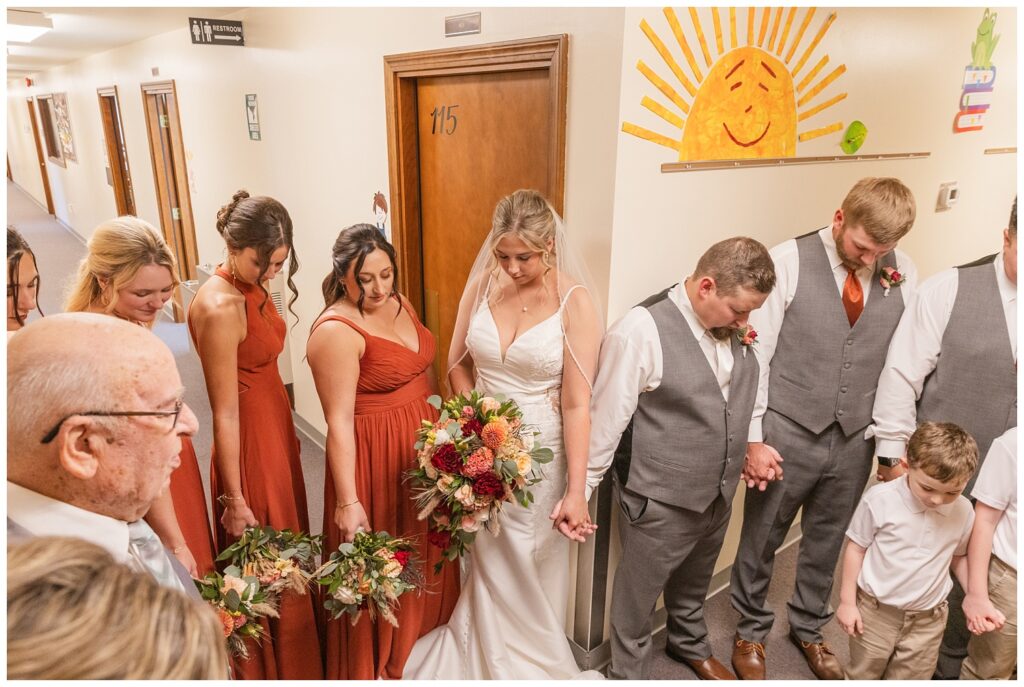 the entire wedding party praying together in the hallway at the church