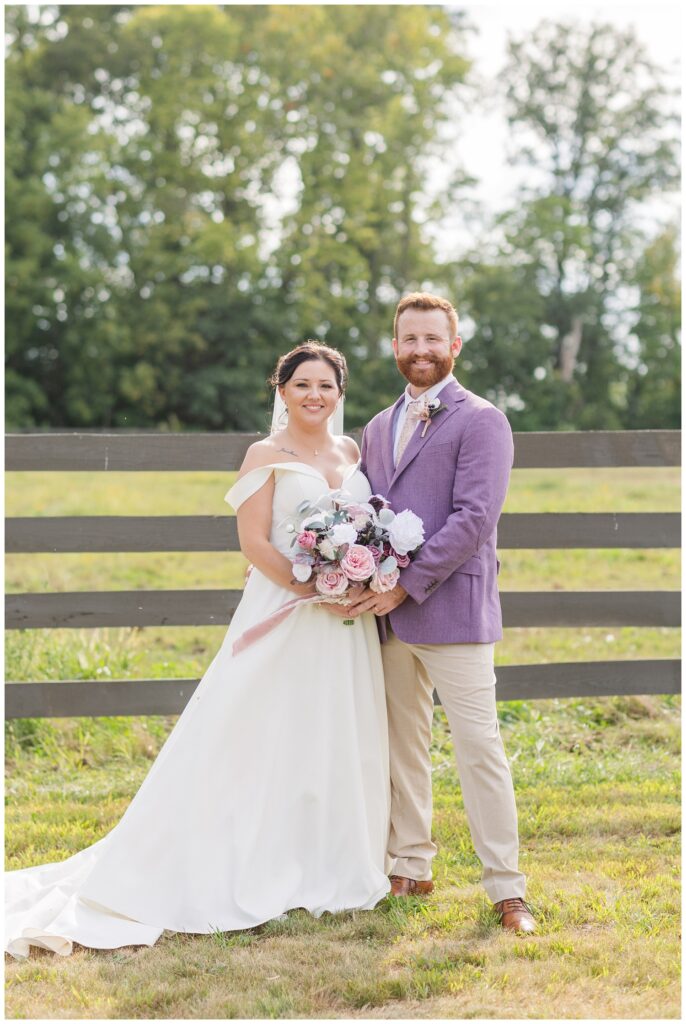 bride and groom posing together in front of a wooden fence for portraits 