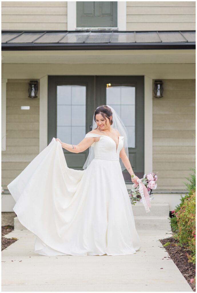 bride holding up her train and posing outside at the Homestead by Stillwaters