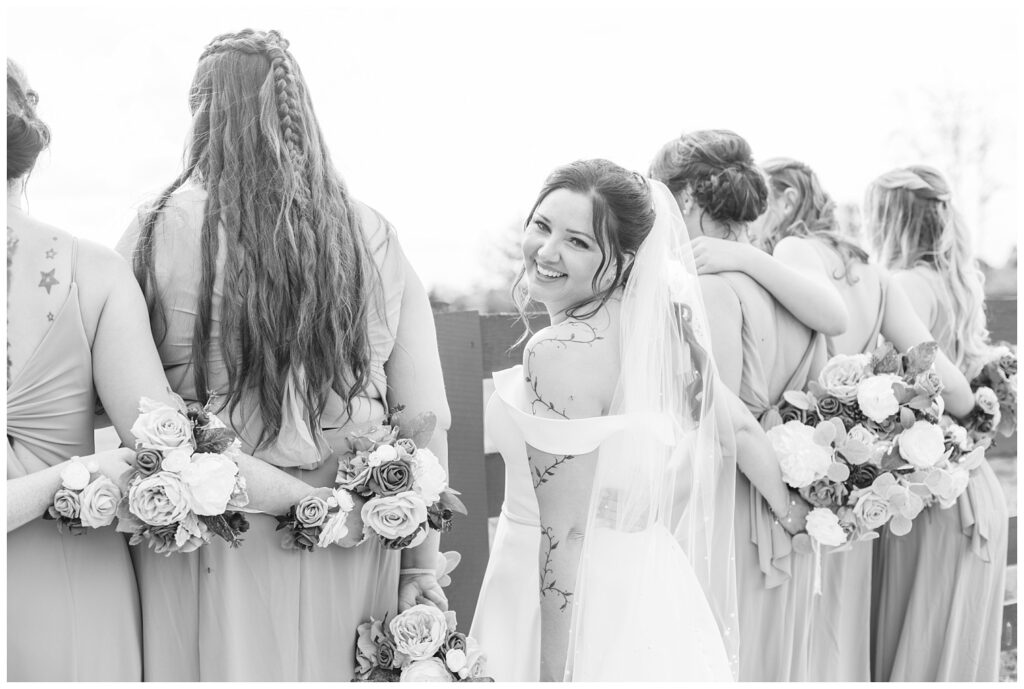 bridesmaids facing towards the fence outside while the bride looks behind