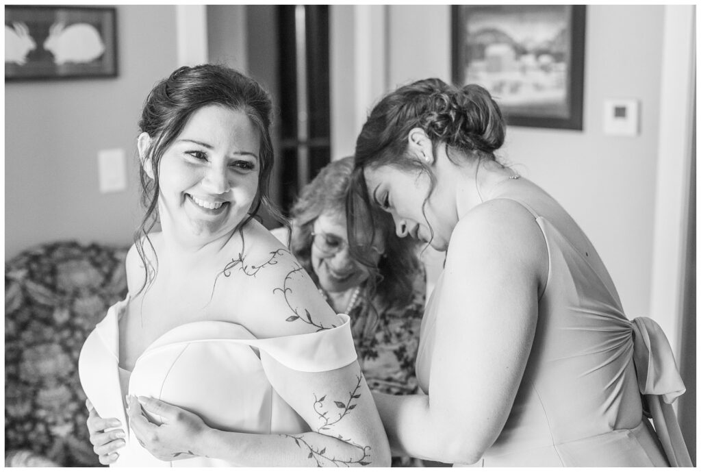 bride's mom and maid of honor zipping her up in her dress while getting ready