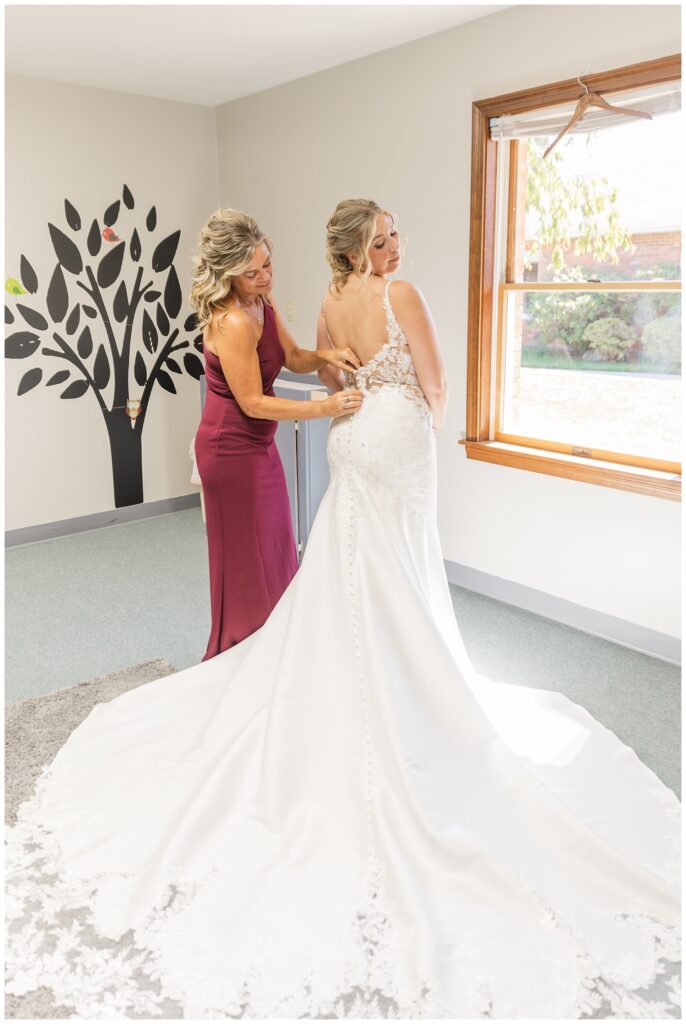 bride's mother zipping up the bride's dress while getting ready at the church