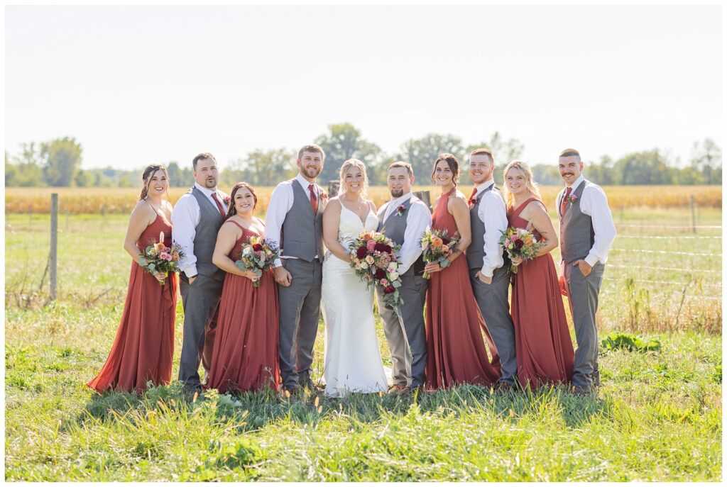 full wedding party posing together in front of a fence on the family dairy farm