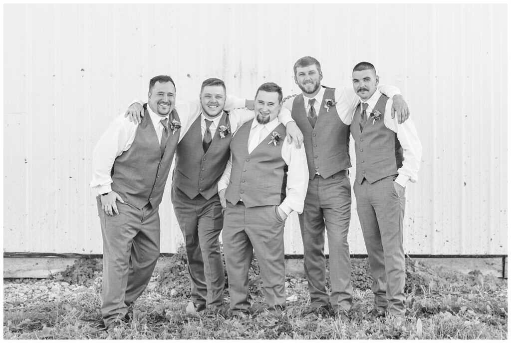 groomsmen with arms wrapped around each other posing in front of a white wall