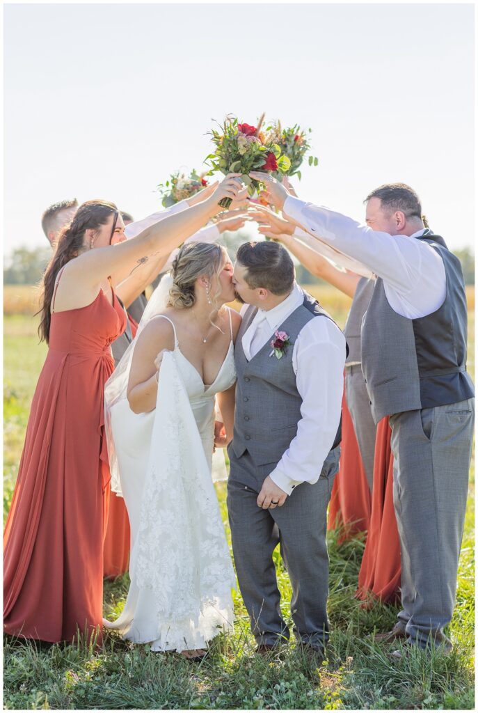 bride and groom kiss after going under an arm tunnel from the wedding party