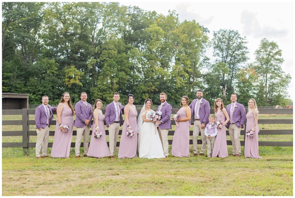 full wedding party posing together along a fence at the Homestead by Stillwaters