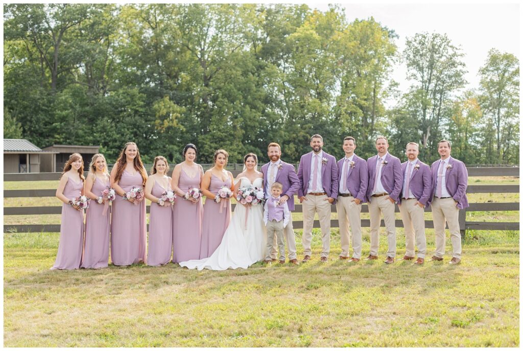 full wedding party smiling in front of a fence at the Homestead by Stillwaters venue in Ohio