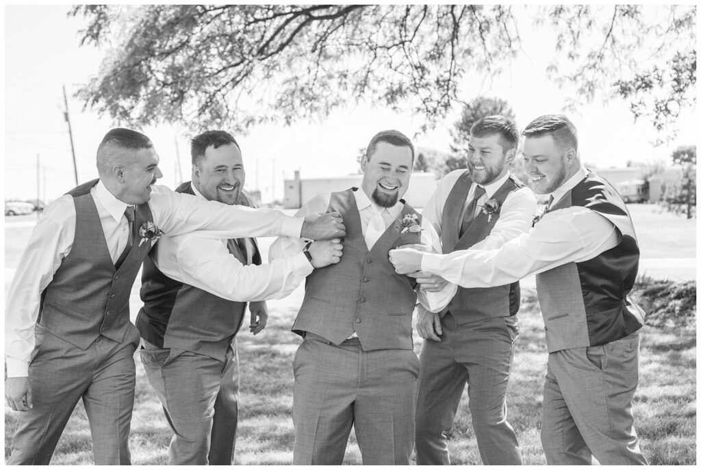 groomsmen pinching the groom and being funny outside 