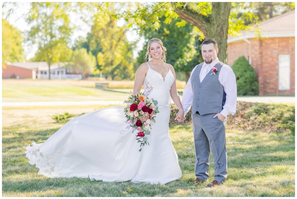 bride and groom holding hands while the bride's train blows in the wind 