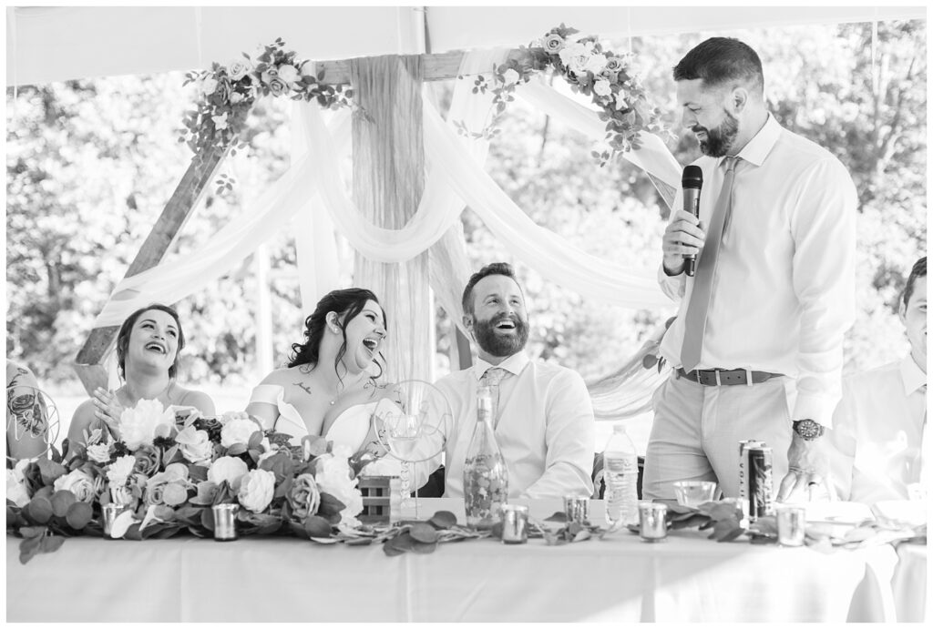 best man sharing his speech at the table during reception making the bride and groom laugh