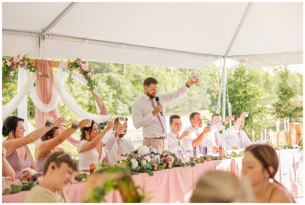 best man asking wedding guests to toast to the bride and groom at reception table