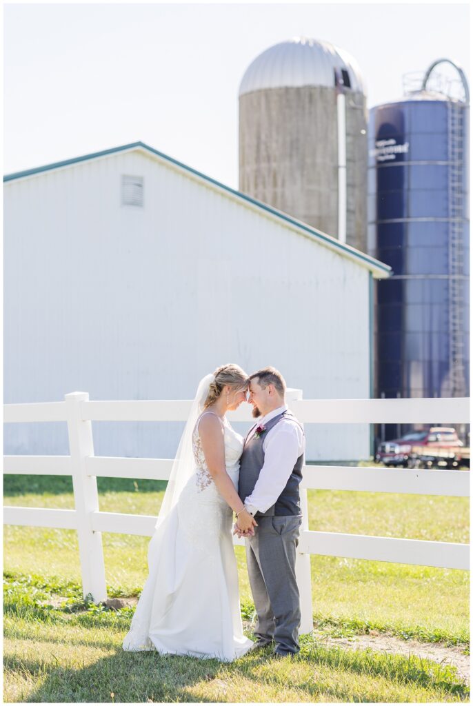 wedding couple facing each other next to a white fence at the dairy farm