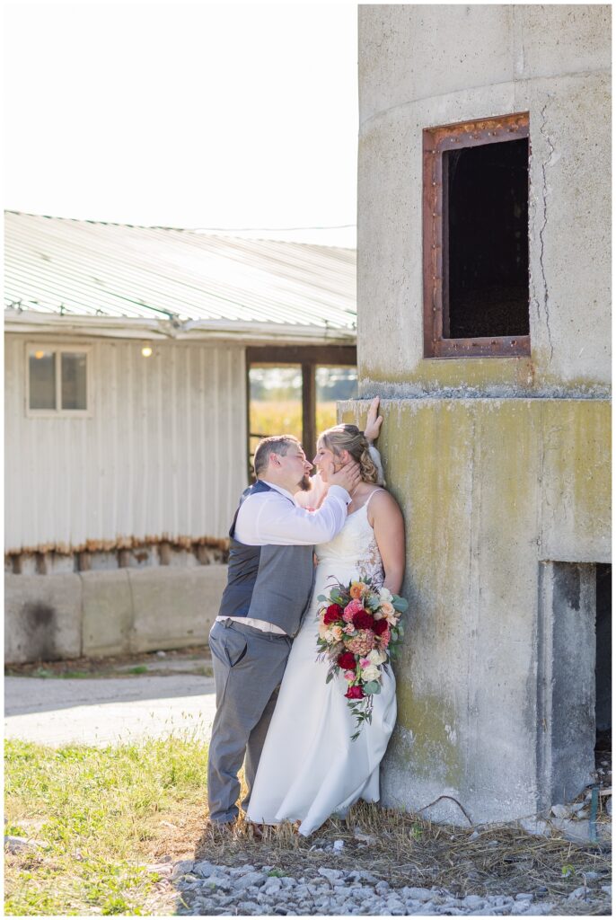 bride leaning against a concrete wall while the groom gives her a kiss