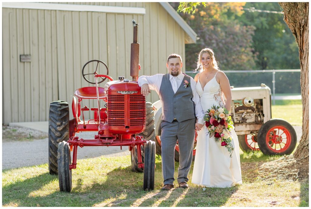 bride and groom smiling while posing against an old red tractor