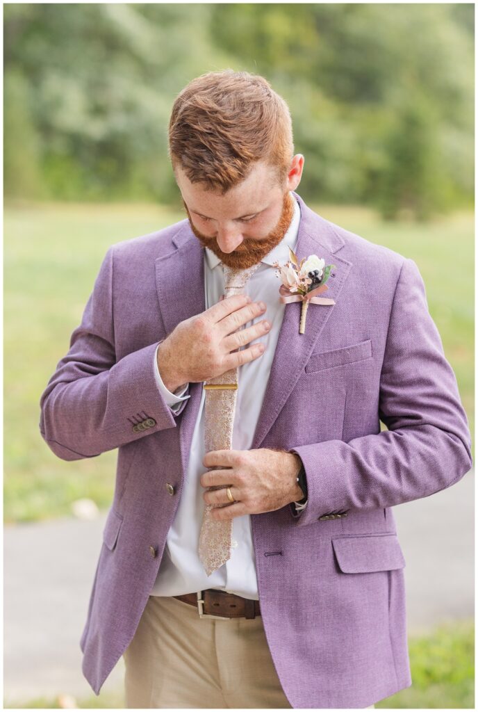 groom adjusting his tie while wearing a lavender blazer and khaki pants