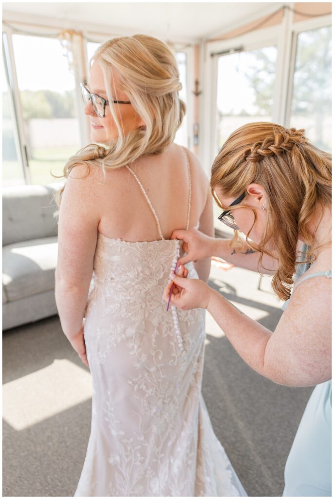 bridesmaid buttoning the back of the bride's lace wedding dress 