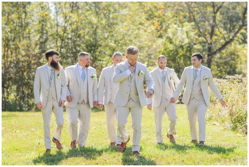 groom walking across the field with the groomsmen following behind at Bradner Preserve