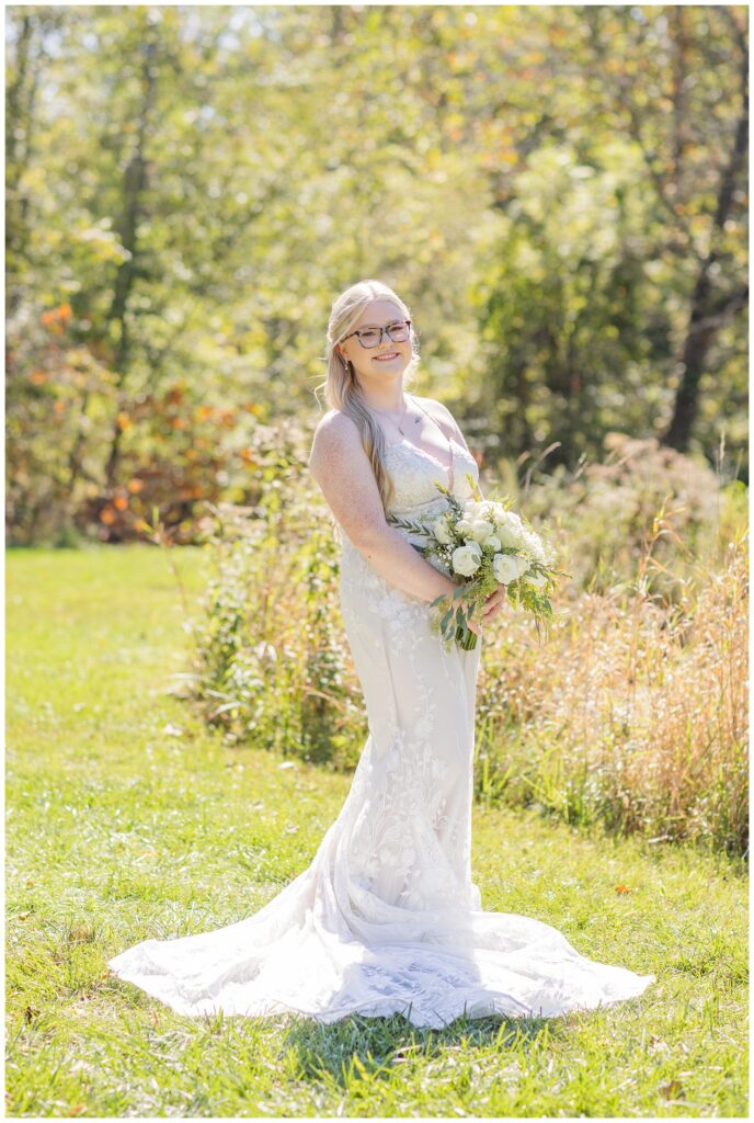 bride posing next to a field holding her bouquet and wearing a lace dress