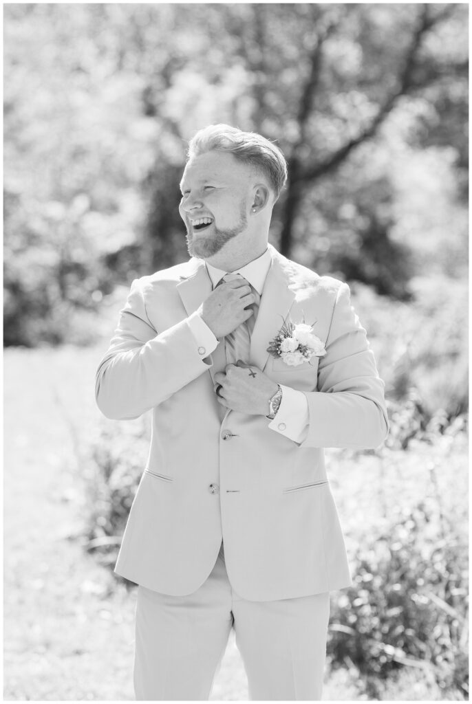 groom adjusting his tie next to tall grass in Bowling Green, Ohio