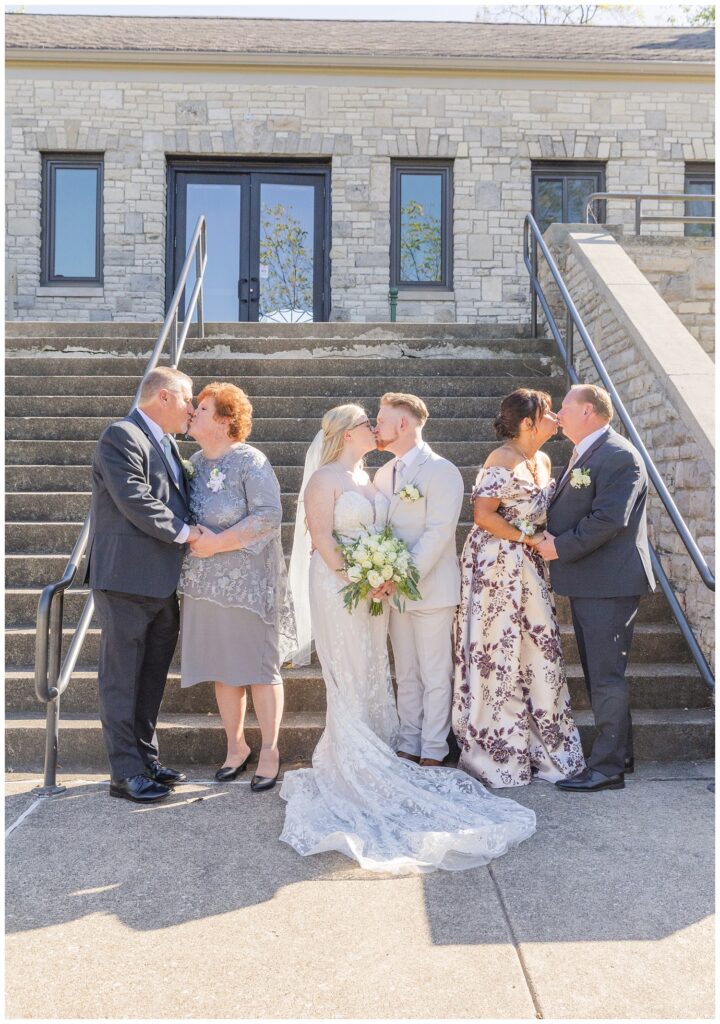 bride and groom and both sets of parents share a kiss outside of Thompson Stone Hall in Ohio