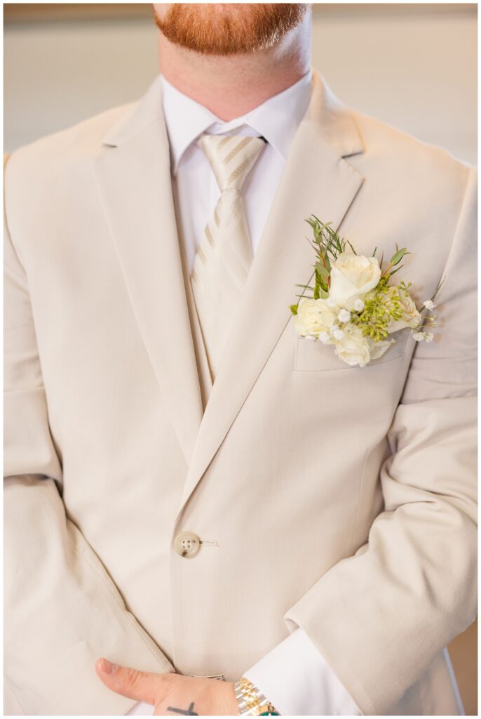 groom wearing a beige suit, striped tie and white rose boutonniere 