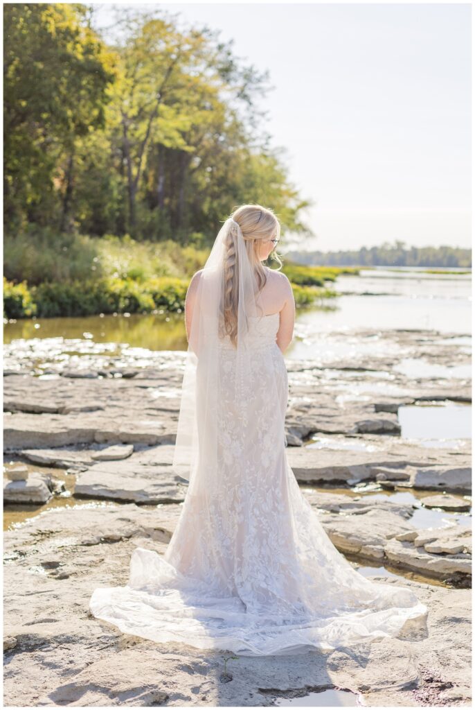 bride showing off the back of her dress while posing next to the river in Bowling Green, Ohio