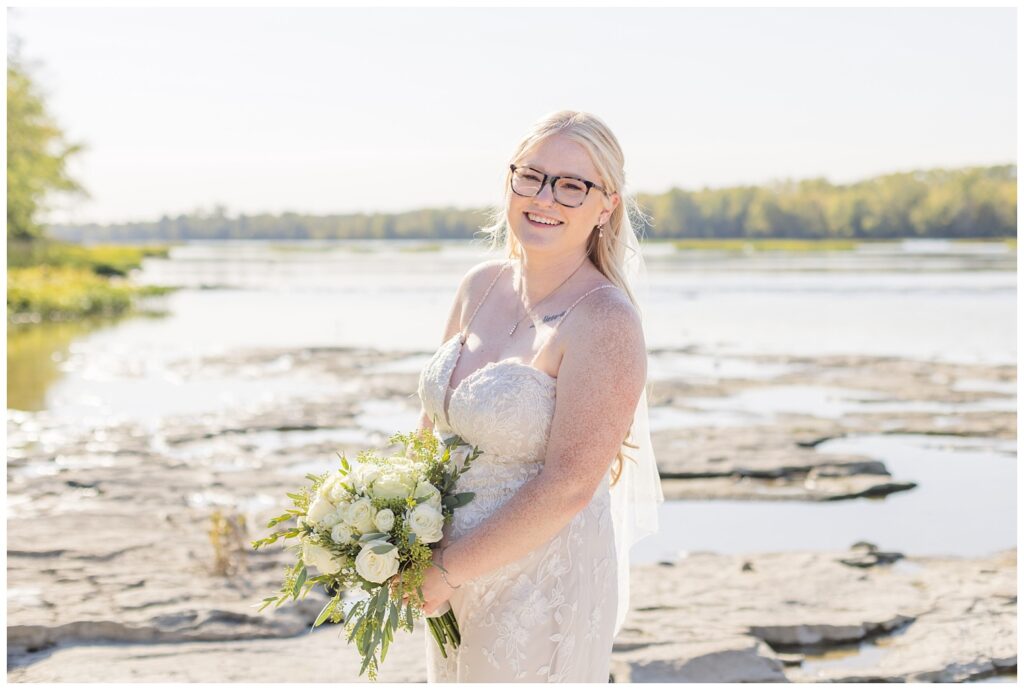 bride leaning towards the camera holding her bouquet next to the Maumee River