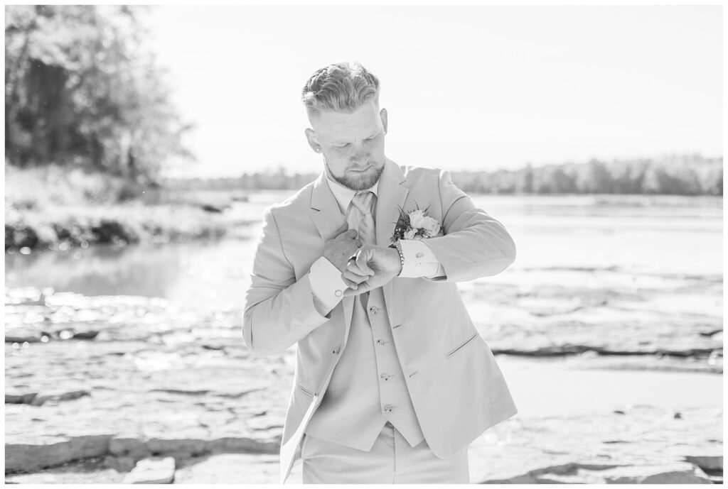 groom checking his watch next to a river at Otsego Park wedding