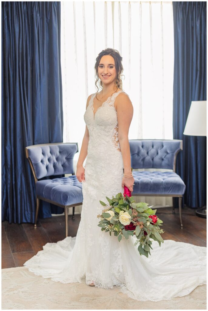 bride posing in the hotel room in front of blue chairs while holding her bouquet