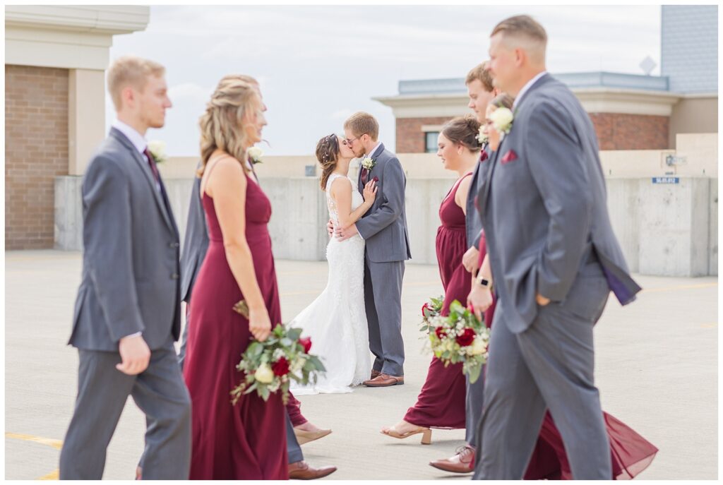 wedding couple sharing a kiss while the bridal party crosses in front of them on top of the parking garage