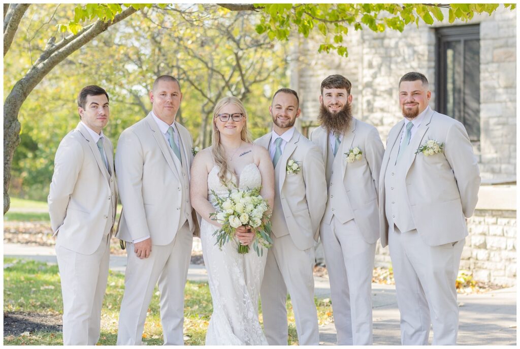 bride posing with the groomsmen under a tree in front of Thompson Stone Hall in Ohio