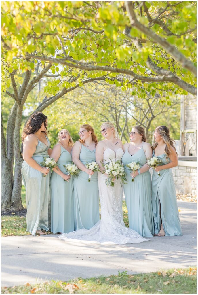 bride and bridesmaids posing under a large tree in Otsego Park after wedding ceremony