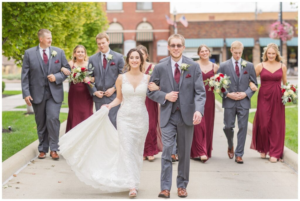 bride and groom walking arm in arm with the wedding party walking behind