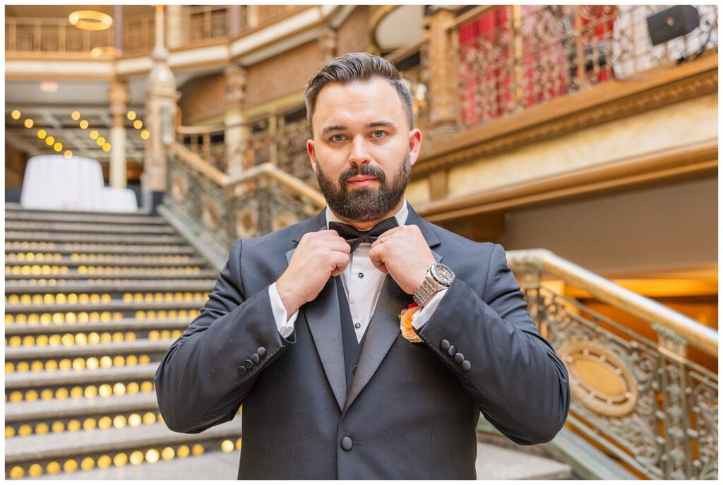 groom adjusting his tie while standing on the bottom of the stairs 