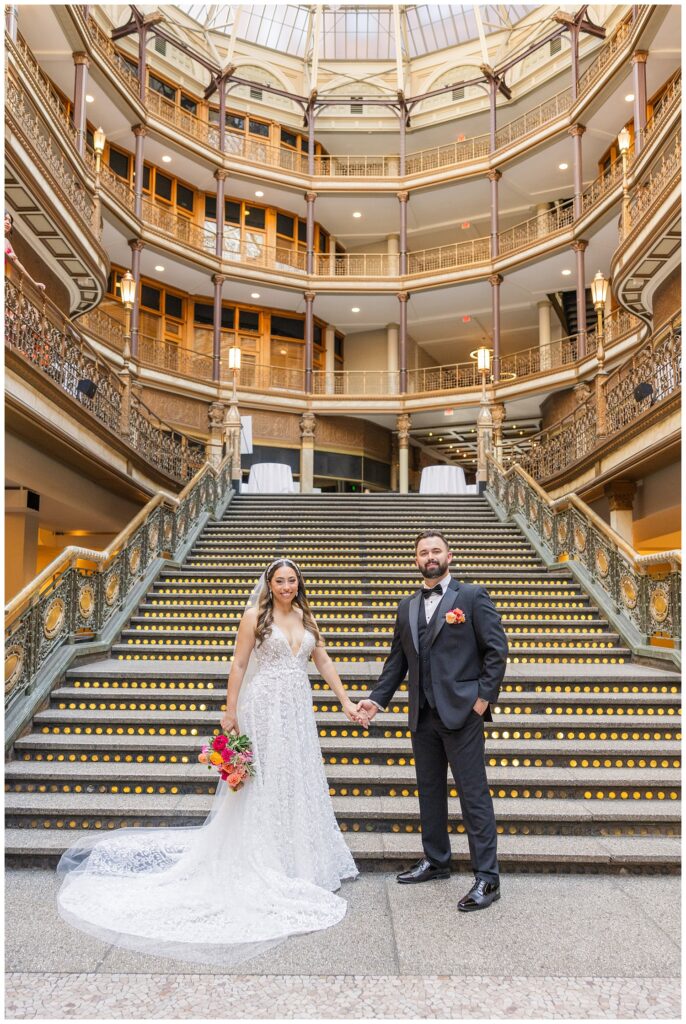 wedding couple holding hands while bride holds bouquet on the the bottom of the stairs