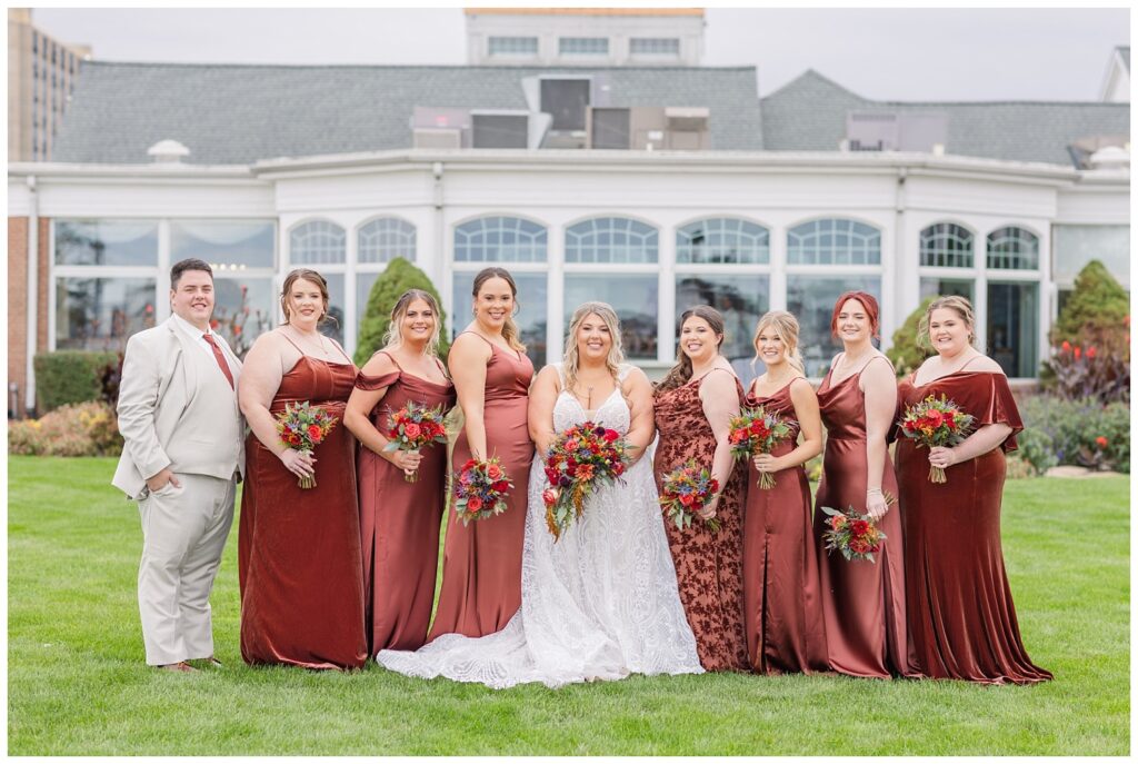 bridal party wearing brown dresses and posing in front of the Sandusky Yacht Club outside