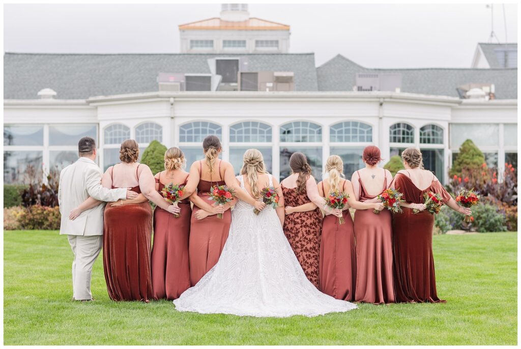 bridal party wearing brown dresses and posing backwards in front of the Sandusky Yacht Club outside