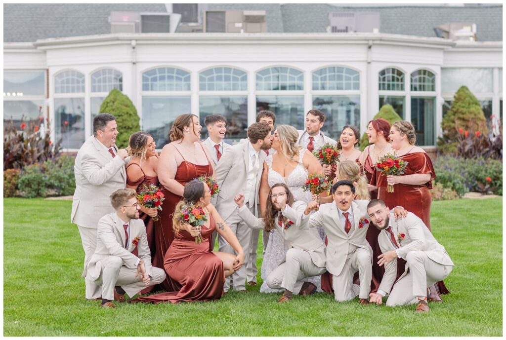 bride and groom share a kiss while the wedding party gathers around them to cheer