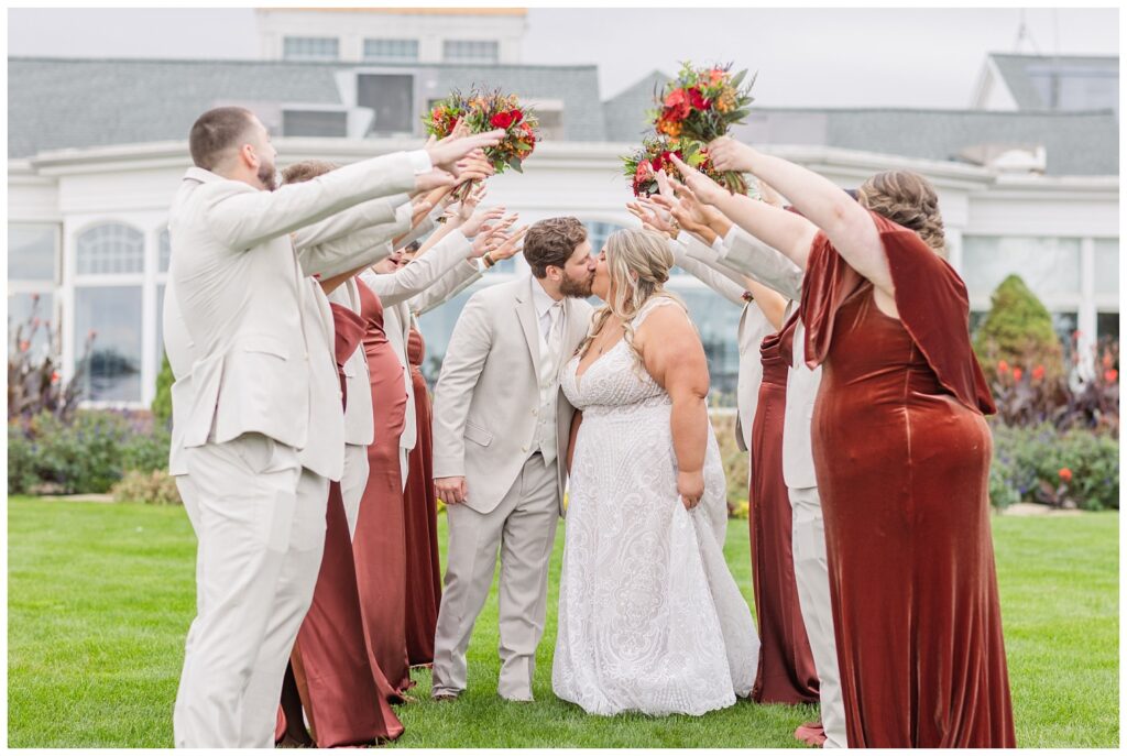 wedding couple kiss while going under a tunnel made by the bridesmaids and groomsmen