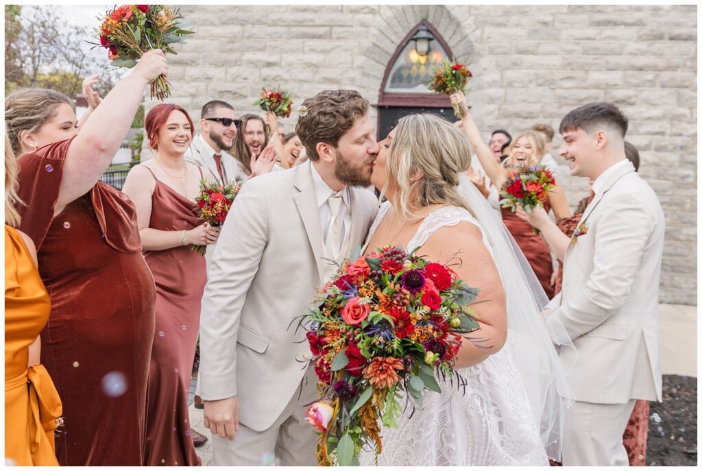 wedding couple kiss while doing a fake exit from the church surrounded by attendants 