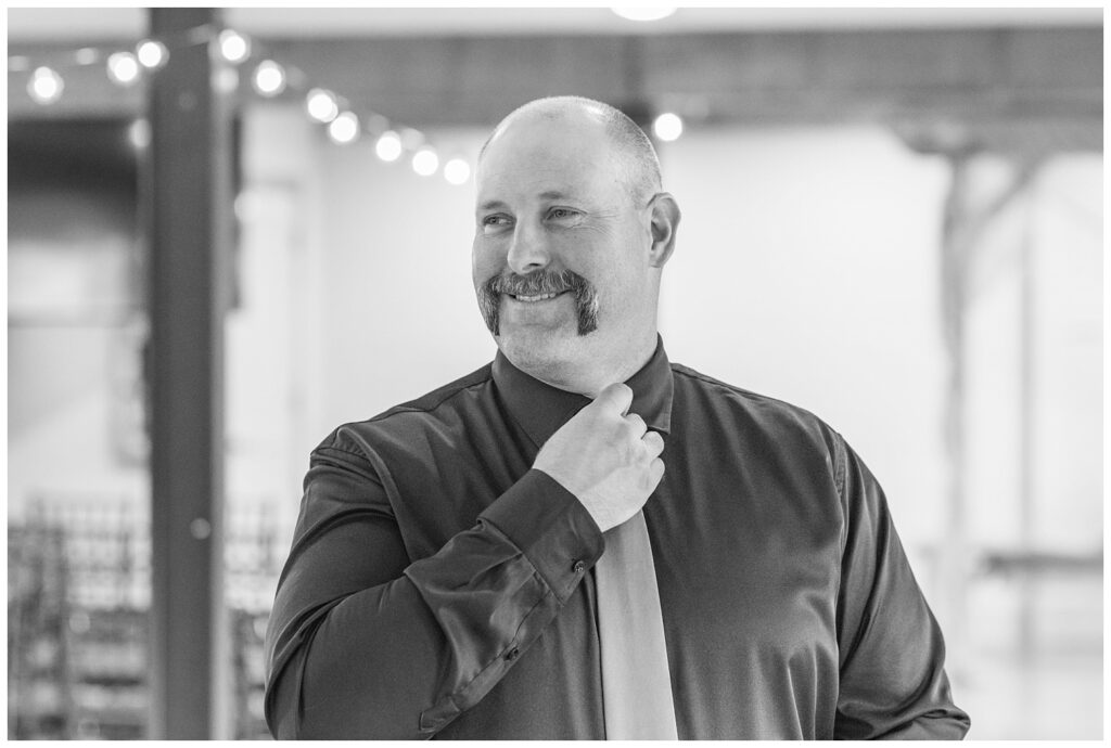 groom adjusting his tie against his black shirt inside before the wedding ceremony