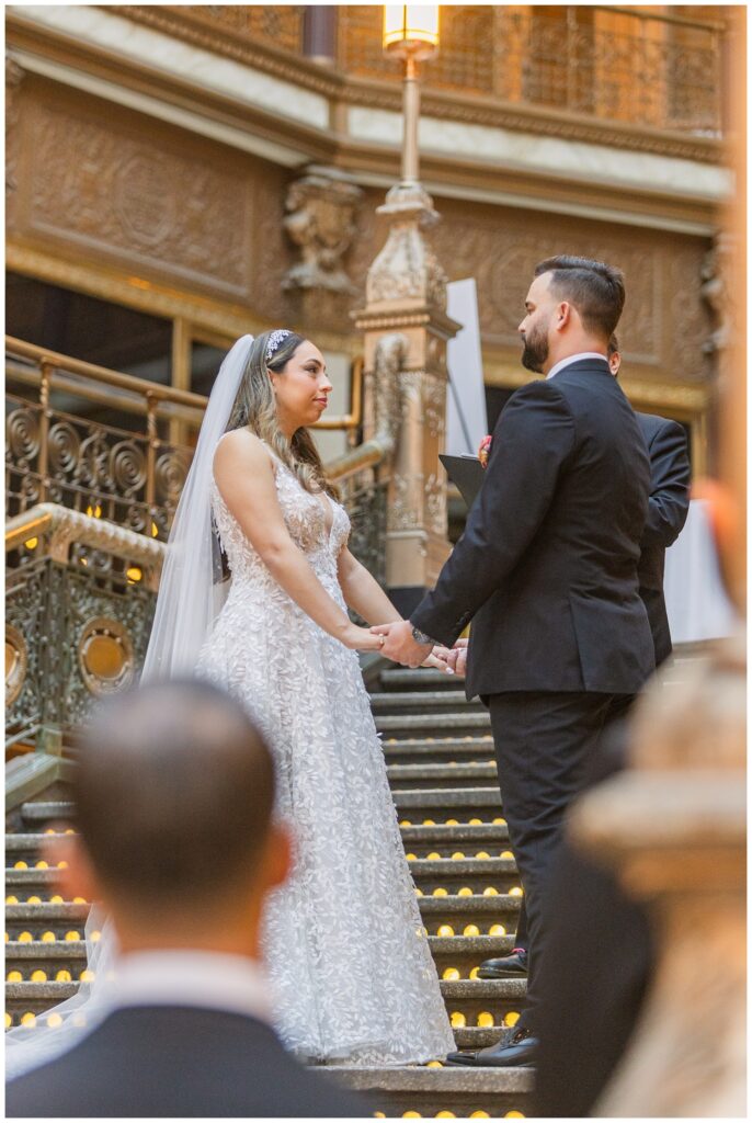 bride and groom holding hands during the ceremony on the stairs at the Arcade