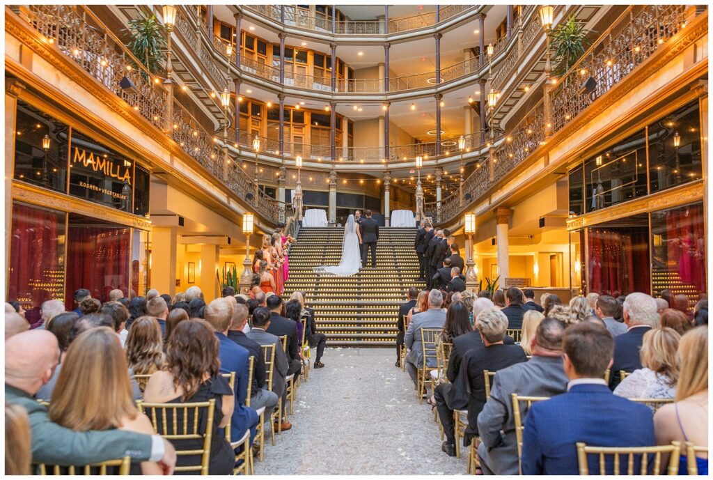 bride and groom standing on the stairs getting married with wedding guests watching from below