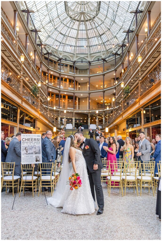 bride and groom kiss at the end of the aisle with the wedding guests behind them