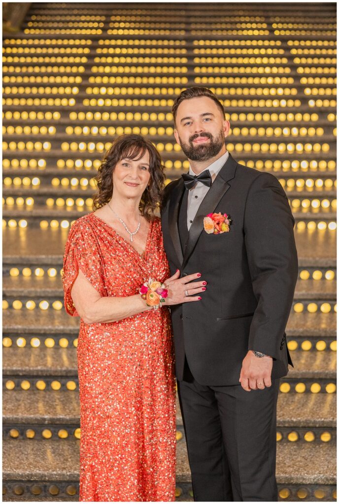 groom posing with his mom at the bottom of the stairs for family portraits