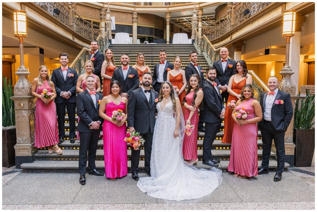 full wedding party posing together on the bottom of the stairs at the Arcade