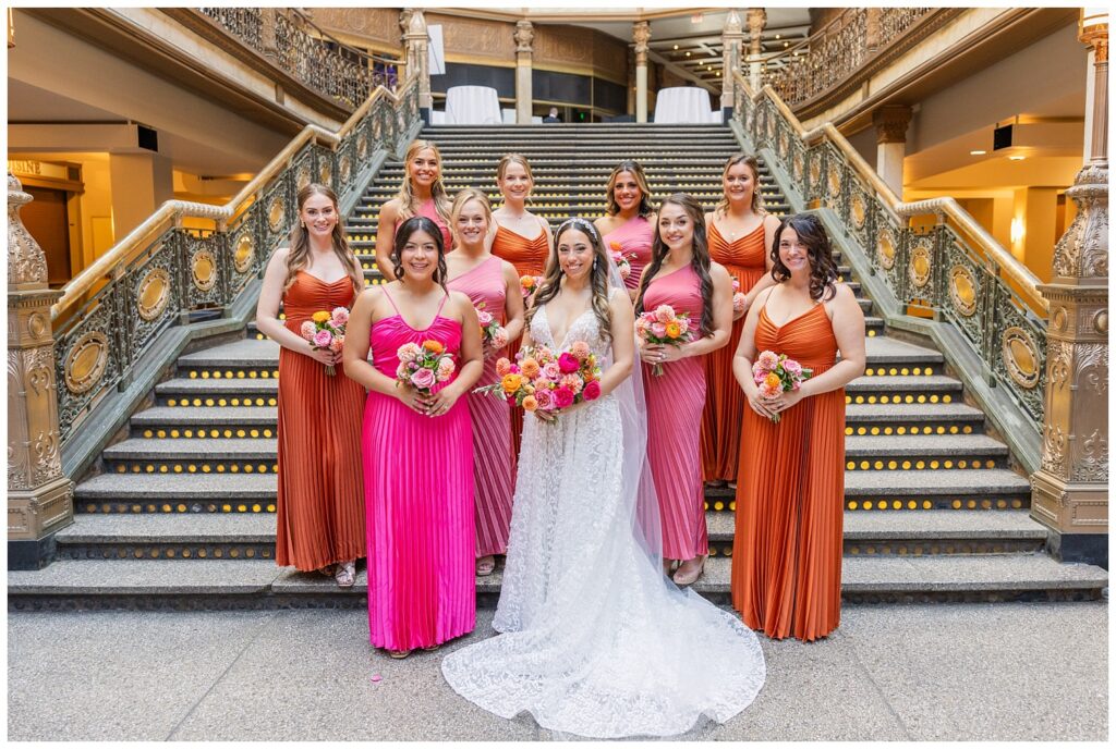 bridal party holding bouquet and posing in rust and pink colored dresses