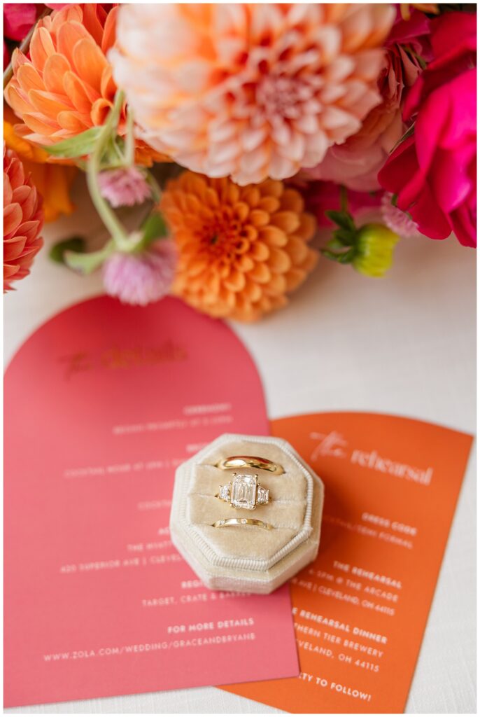 wedding rings sitting in a ring box on top of pink and orange invitation suite