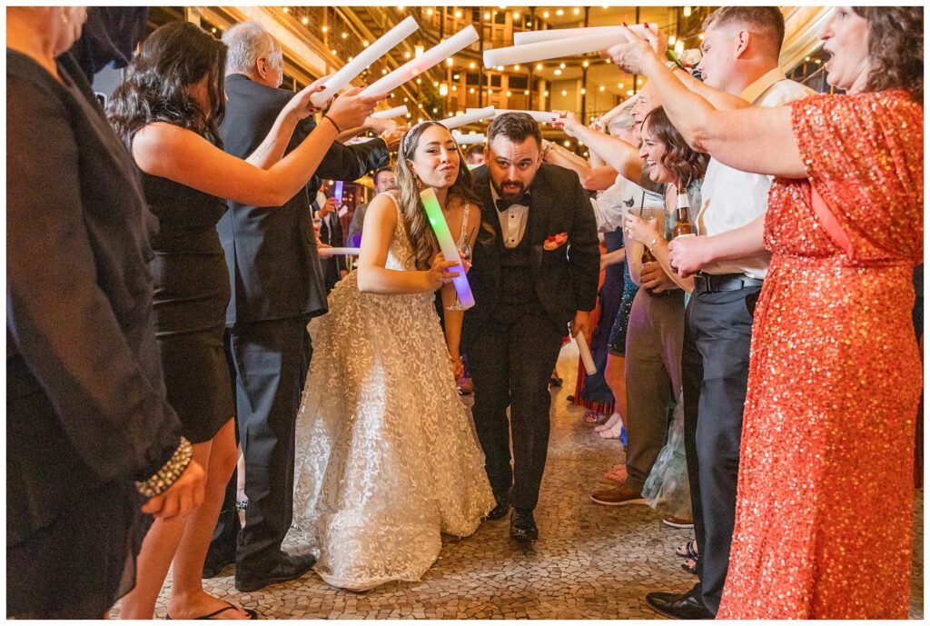 wedding couple walking under guests arms while holding light up wands 