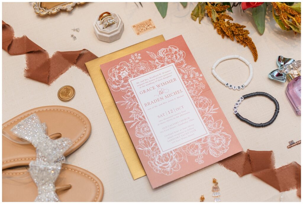 wedding flat lay with invitation suite, bride's sandals, brown ribbon and rings